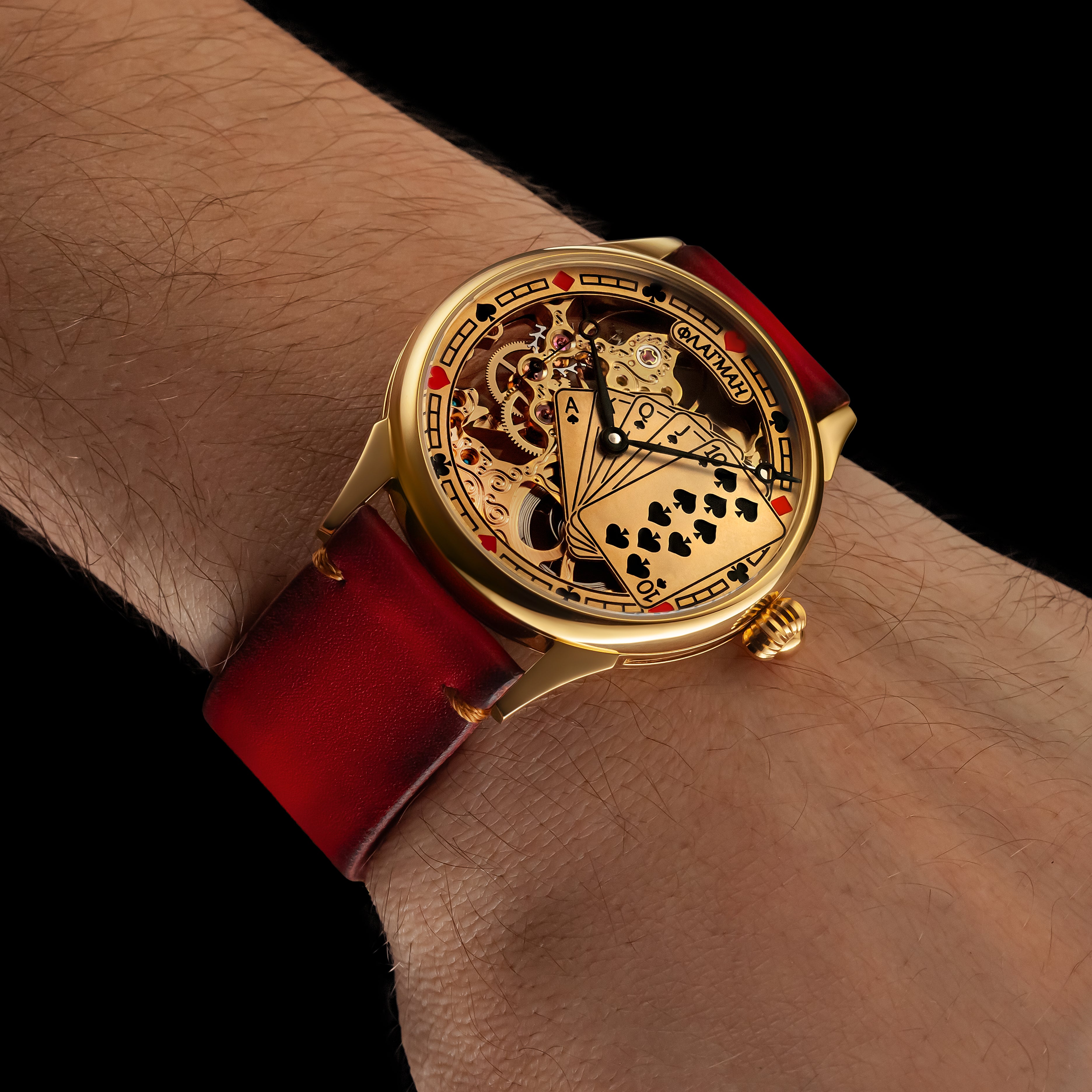 Gold watch with red strap on a wrist against a black background