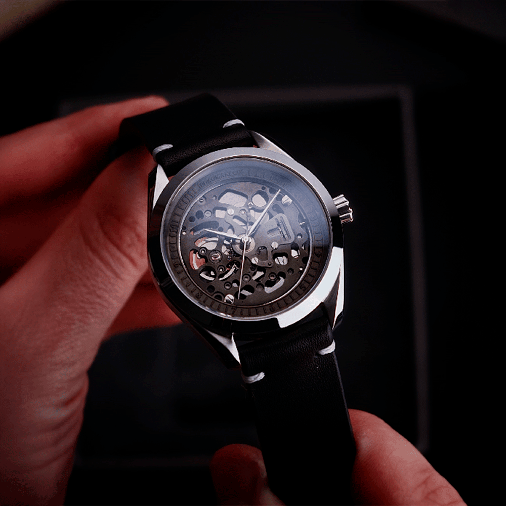 Person holding a black wristwatch with a visible mechanical inner workings against a dark background