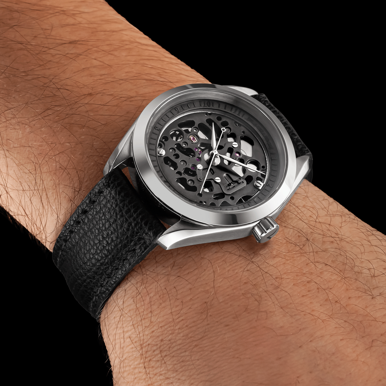 Handmade wristwatch with black strap on a wrist against a black background