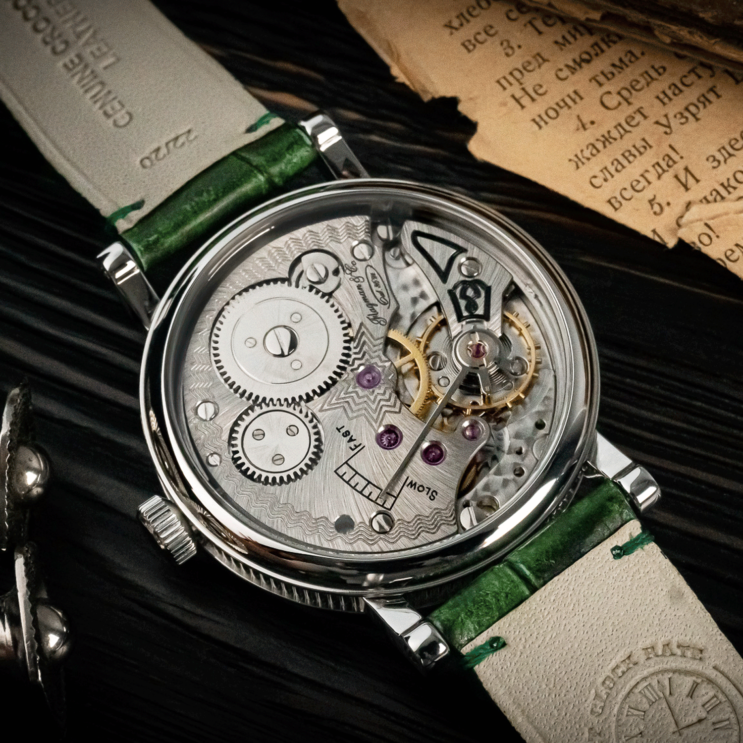 Artisan Watch with green leather strap and visible mechanical components on a dark surface.