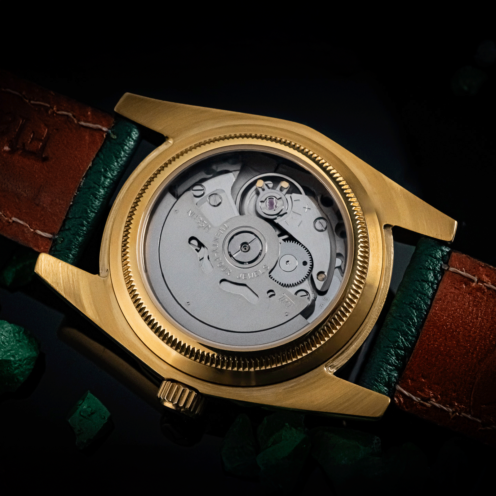 Gold mechanical watch with a green leather strap on a dark background