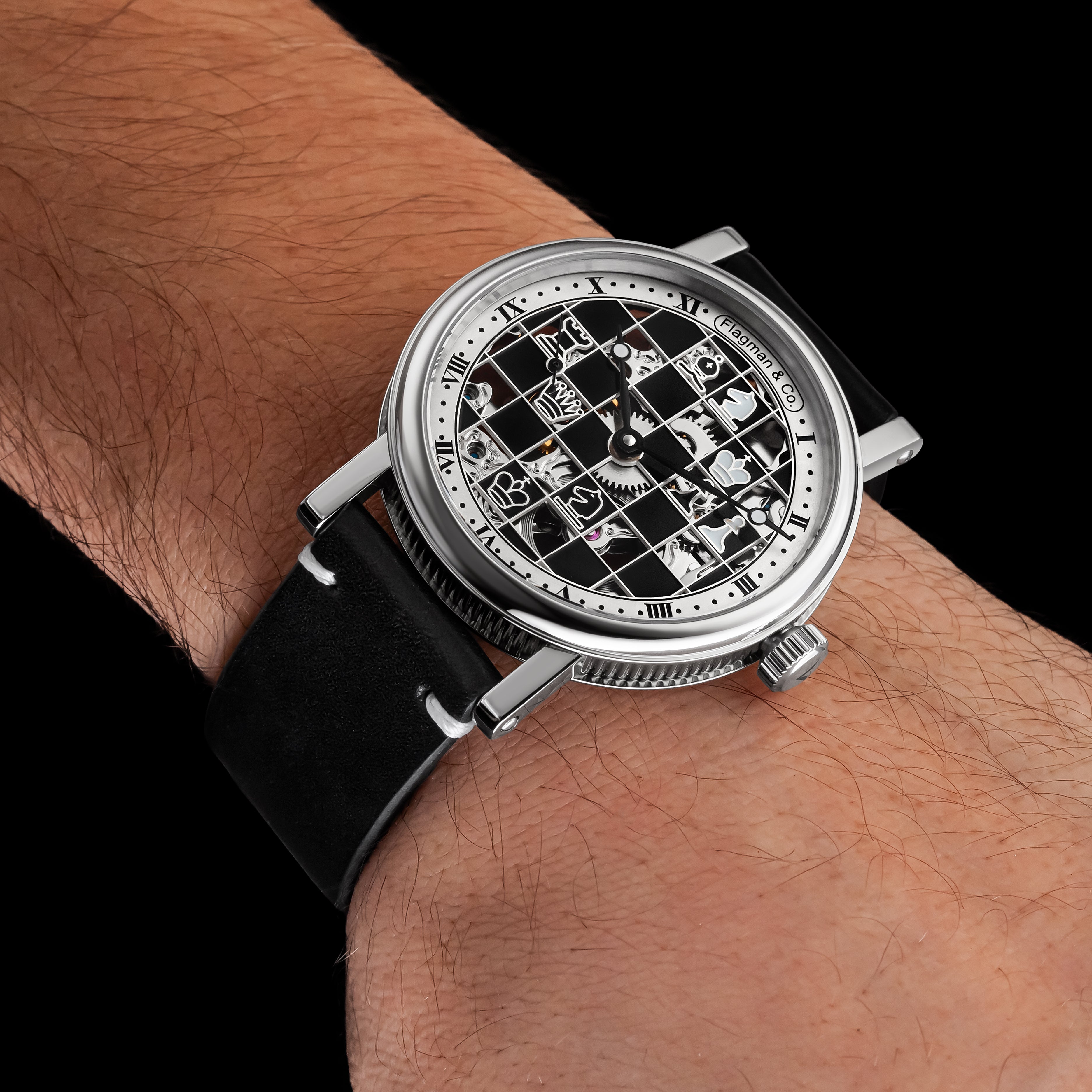 Luxury watch with black leather strap on a wrist against a black background